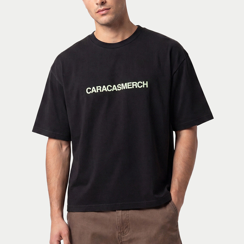 Man wearing the black Caracasmerch boxy t-shirt with the white chest wordmark and brown trousers